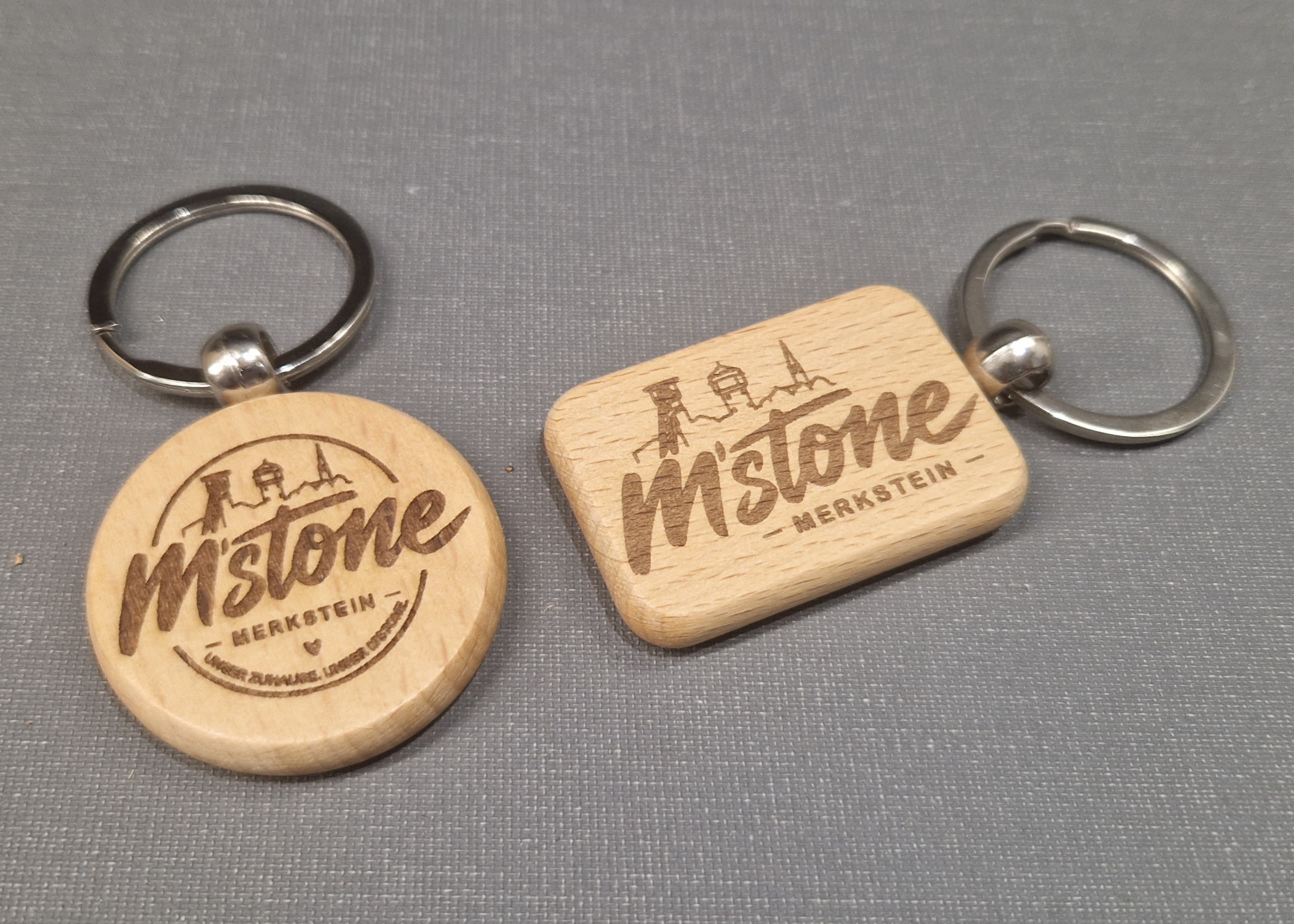 Zwei M'stone Schlüsselanhänger aus Holz, rund und eckig, mit Gravur